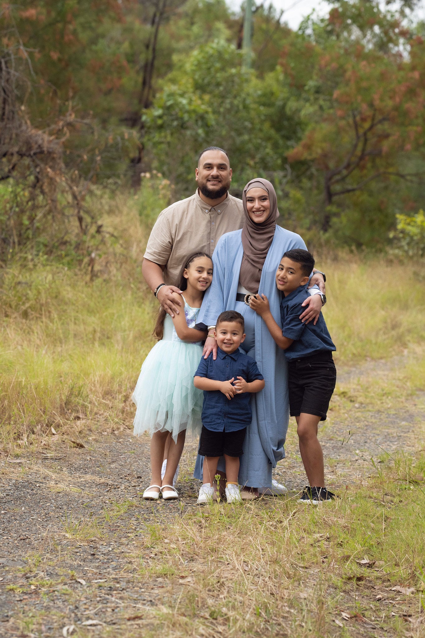 A family of five standing outdoors, with two adults and three children, posing for a photo.