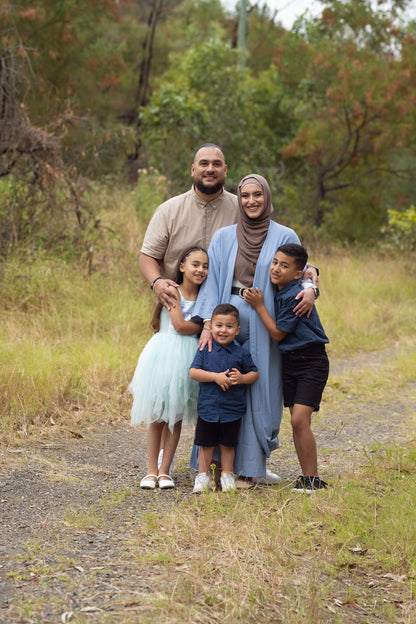 A family of five standing outdoors, with two adults and three children, posing for a photo.