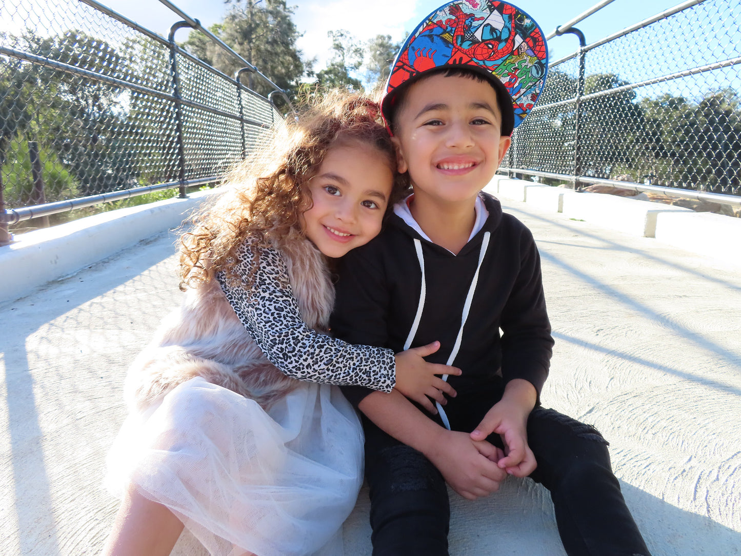 A child counselling session with a young girl and a boy smiling and sitting close by a metal railing with trees in the background.
