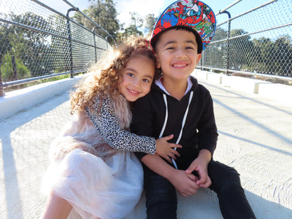 A child counselling session with a young girl and a boy smiling and sitting close by a metal railing with trees in the background.