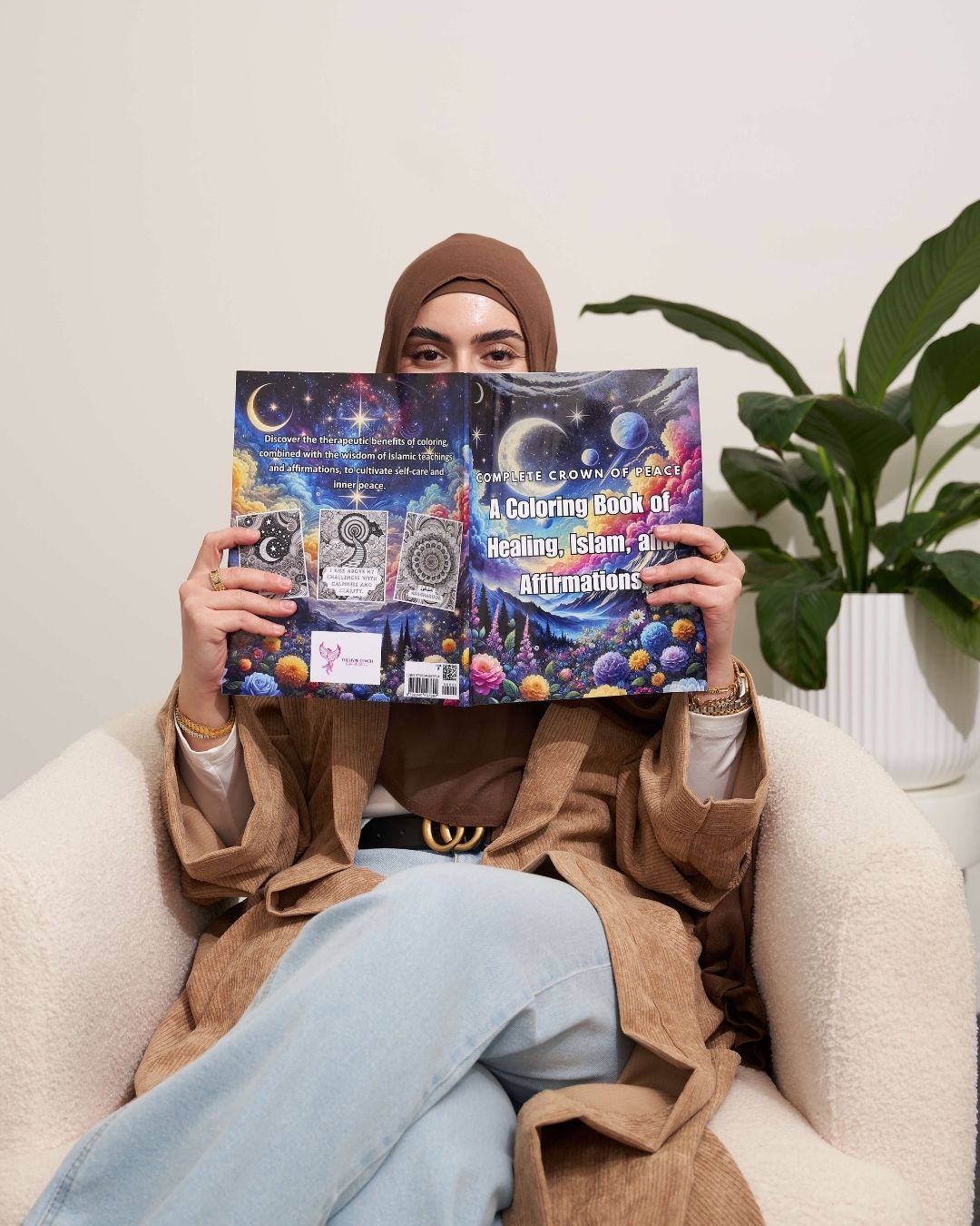 Person holding a coloring book titled 'A Coloring Book of Healing Islamic Affirmations' in front of their face, sitting on a couch.